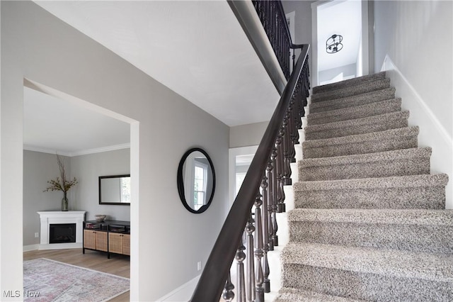 staircase featuring crown molding, baseboards, wood finished floors, and a fireplace