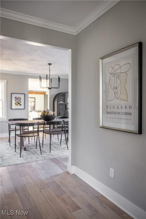 dining space featuring crown molding, baseboards, an inviting chandelier, and wood-type flooring