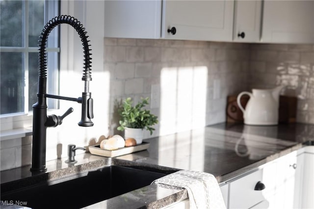 kitchen featuring a sink, dark stone counters, backsplash, and white cabinets