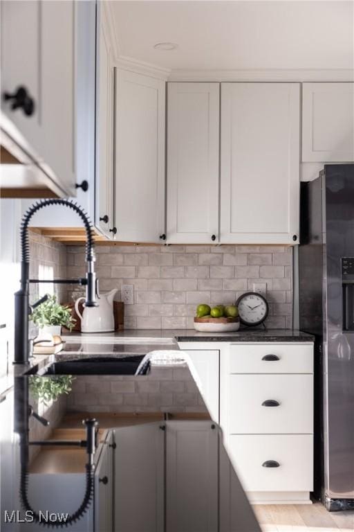 kitchen with white cabinets, dark countertops, a sink, fridge with ice dispenser, and tasteful backsplash