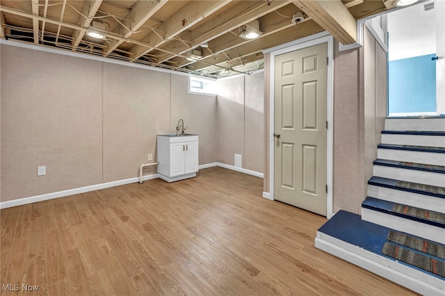 basement with a sink, baseboards, light wood-type flooring, and stairs
