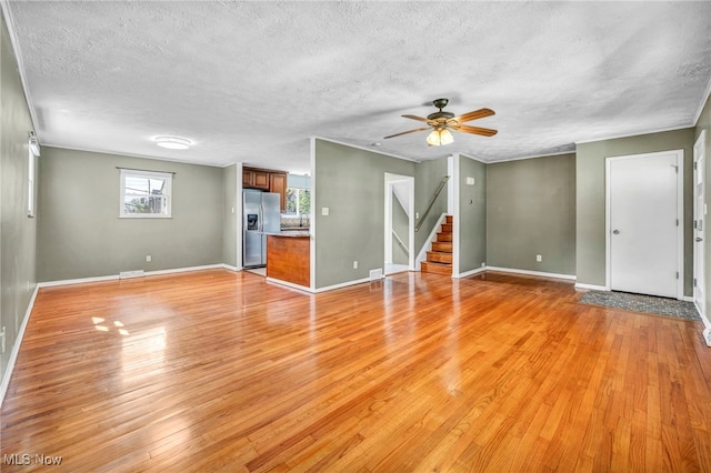unfurnished living room with stairway, baseboards, ceiling fan, and light wood-style floors