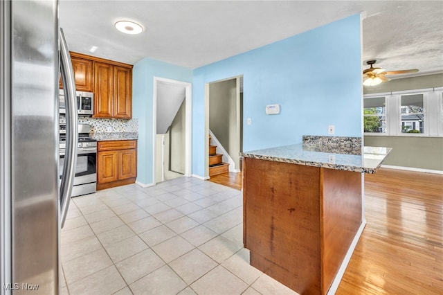 kitchen with brown cabinetry, a peninsula, baseboards, a ceiling fan, and stainless steel appliances
