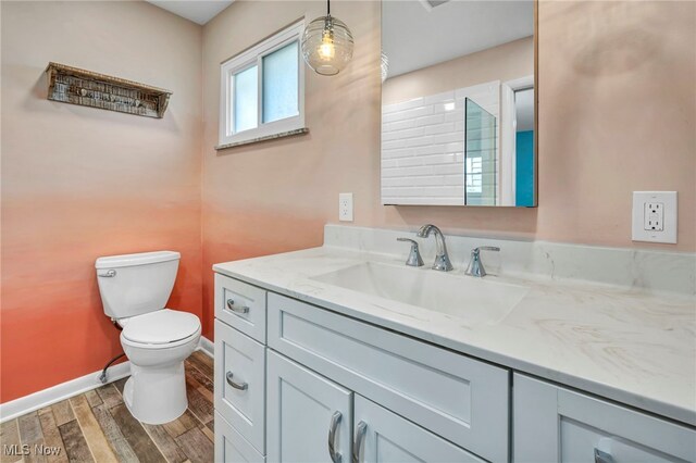bathroom featuring toilet, baseboards, wood finished floors, and vanity