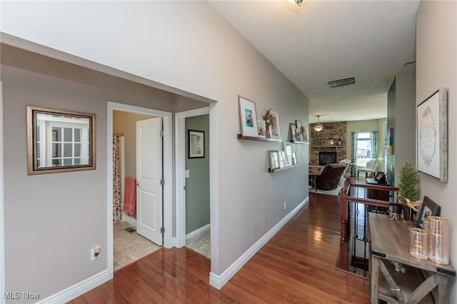 corridor with a textured ceiling, baseboards, visible vents, and wood finished floors