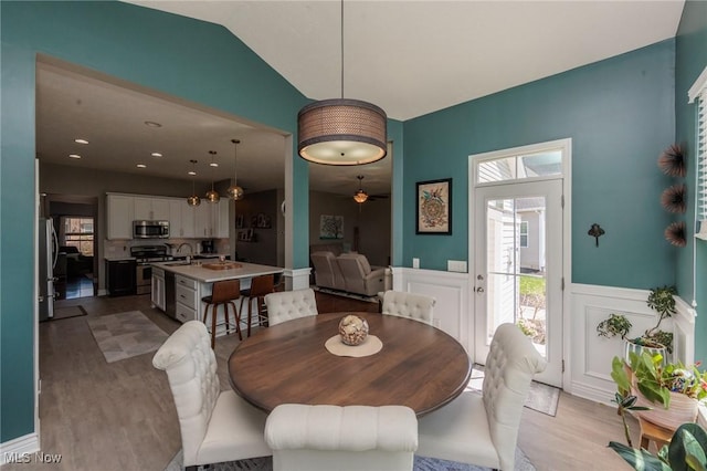 dining space featuring light wood-type flooring, a decorative wall, and a wainscoted wall