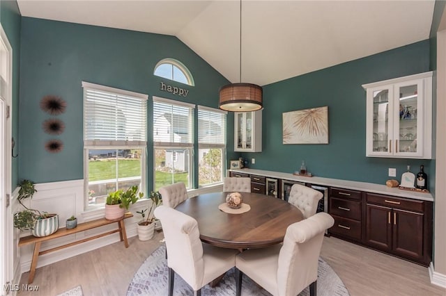 dining room featuring light wood-style floors, wainscoting, and vaulted ceiling