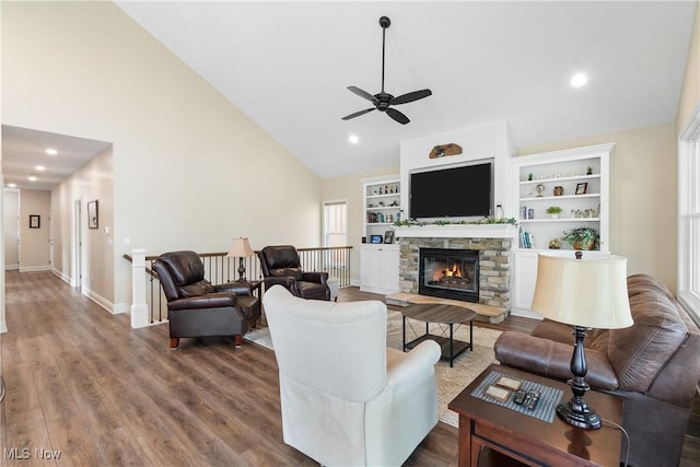 living area featuring a ceiling fan, a stone fireplace, wood finished floors, high vaulted ceiling, and baseboards