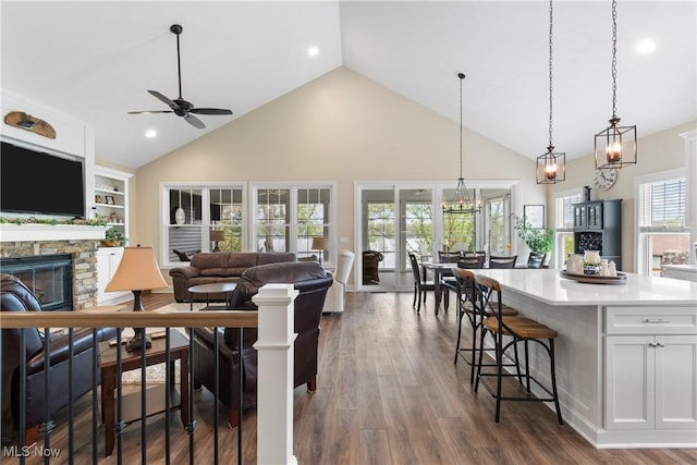 living room with ceiling fan, a stone fireplace, high vaulted ceiling, dark wood-style floors, and recessed lighting