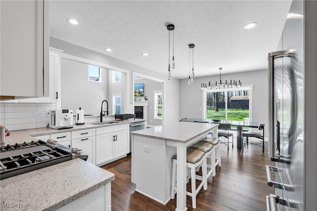 kitchen featuring a center island, light stone countertops, a sink, white cabinets, and recessed lighting