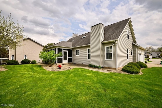back of house featuring a garage, a yard, a chimney, and a sunroom