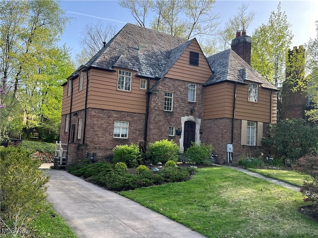 tudor home featuring brick siding, a front yard, a high end roof, and a chimney