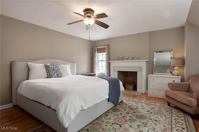 bedroom with a fireplace, a ceiling fan, and wood finished floors