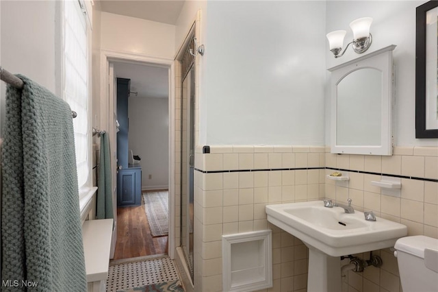 full bathroom with tile walls, a wainscoted wall, a shower with door, and toilet