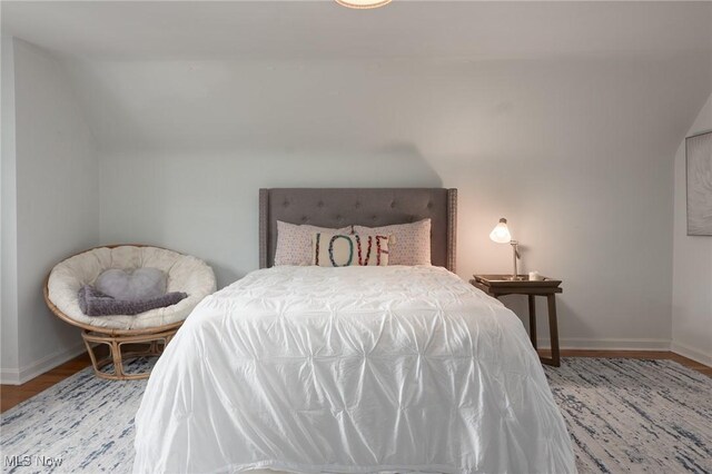 bedroom featuring baseboards, wood finished floors, and lofted ceiling