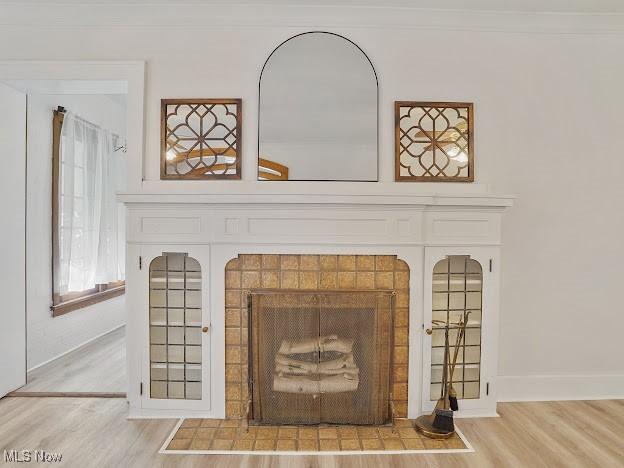 interior details with a tiled fireplace, baseboards, crown molding, and wood finished floors