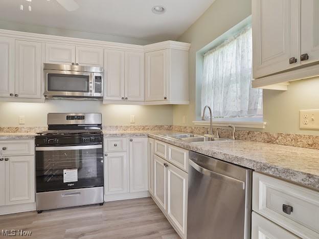 kitchen with light wood-type flooring, light countertops, white cabinets, a sink, and stainless steel appliances