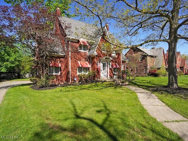 view of front of property featuring a chimney, a front lawn, and brick siding