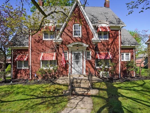tudor-style house with a chimney, a front lawn, and brick siding