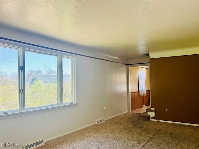 carpeted spare room featuring a textured ceiling, baseboards, and visible vents