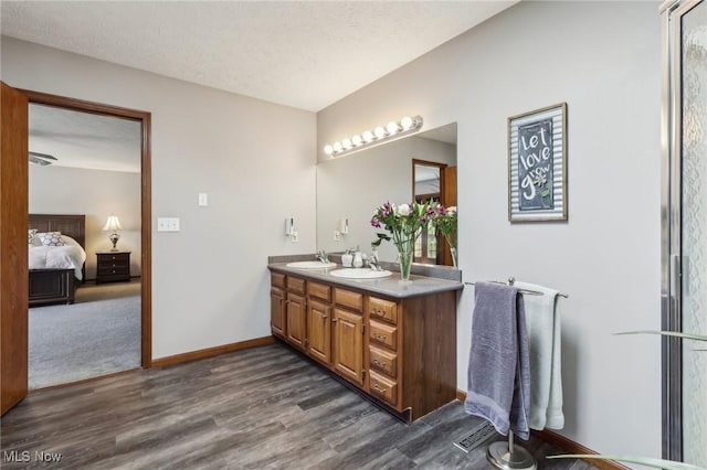 ensuite bathroom featuring connected bathroom, double vanity, a sink, and wood finished floors