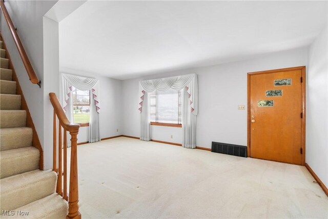 carpeted foyer entrance featuring visible vents, baseboards, and stairway