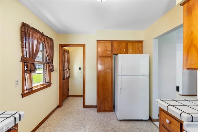 kitchen with baseboards, freestanding refrigerator, tile countertops, and brown cabinets
