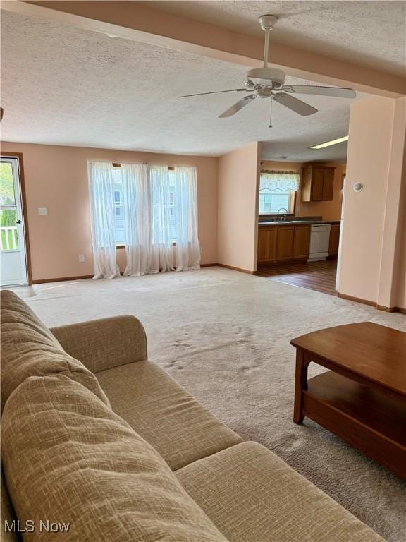 living area with baseboards, a textured ceiling, and light carpet