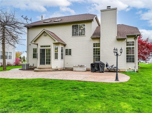 rear view of house featuring a chimney, roof with shingles, central AC, a yard, and a patio