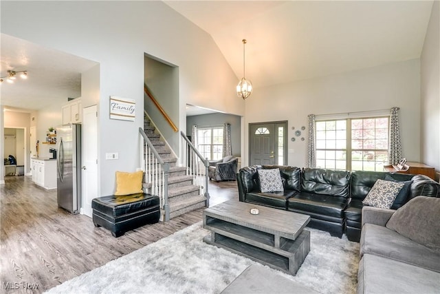 living area with stairway, high vaulted ceiling, light wood-style floors, and a healthy amount of sunlight