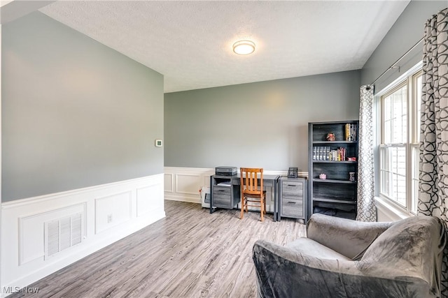 office with a decorative wall, visible vents, wainscoting, and light wood-type flooring