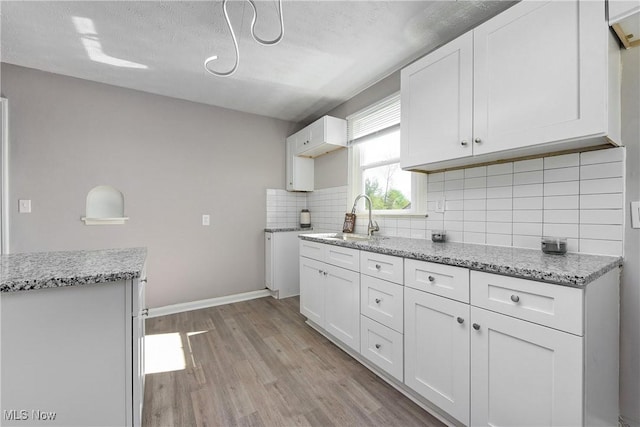 kitchen featuring a sink, light wood-style flooring, decorative backsplash, and white cabinets