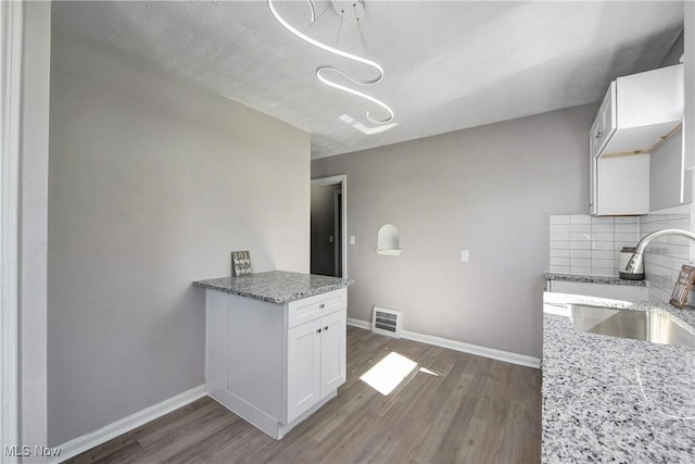 kitchen with decorative backsplash, visible vents, light stone countertops, wood finished floors, and a sink