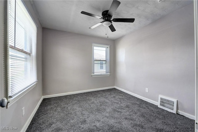empty room with ceiling fan, a textured ceiling, dark colored carpet, baseboards, and visible vents