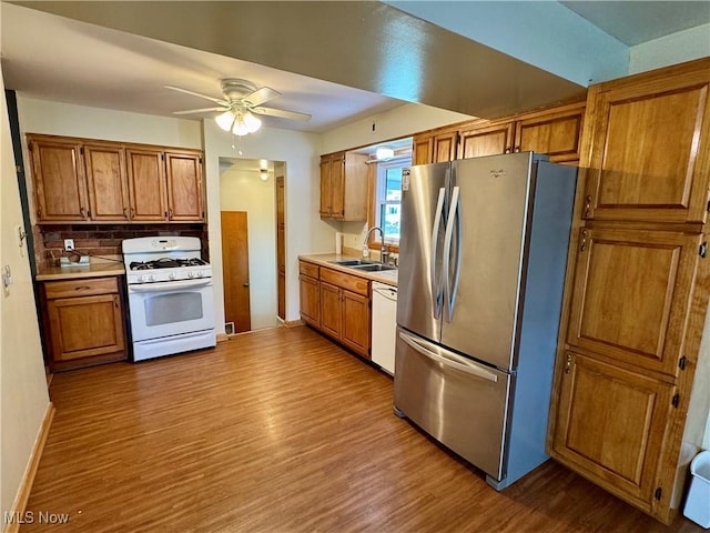 kitchen with wood finished floors, white appliances, light countertops, brown cabinets, and a sink