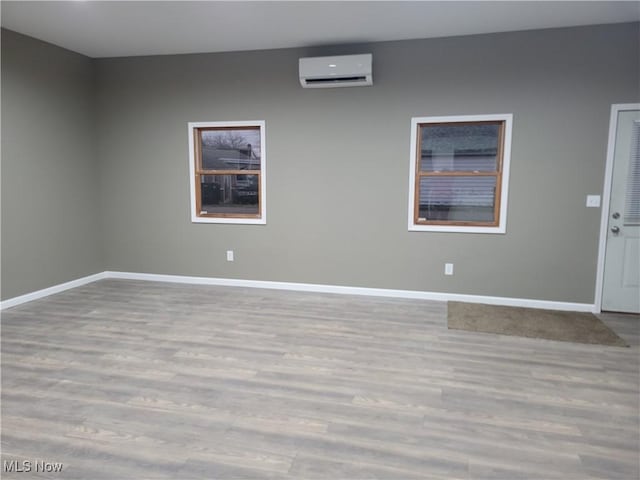 empty room featuring baseboards, a wall unit AC, and wood finished floors