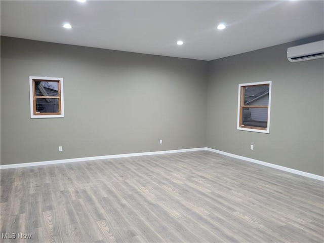 spare room featuring recessed lighting, baseboards, light wood finished floors, and a wall mounted air conditioner