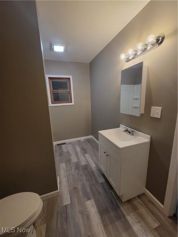 half bathroom featuring vanity, baseboards, wood finished floors, and toilet