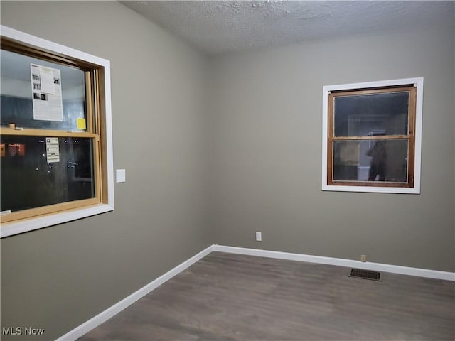 spare room with baseboards, a textured ceiling, wood finished floors, and visible vents
