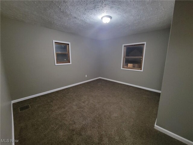 unfurnished room with visible vents, a textured ceiling, baseboards, and dark colored carpet