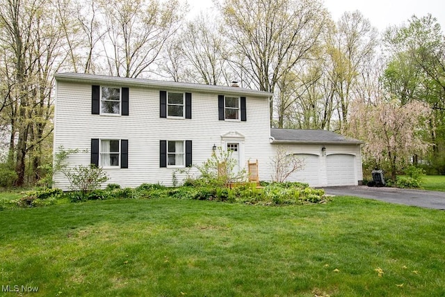 colonial house with an attached garage, driveway, a chimney, and a front lawn