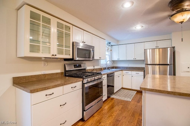 kitchen with a sink, appliances with stainless steel finishes, wood finished floors, and white cabinetry
