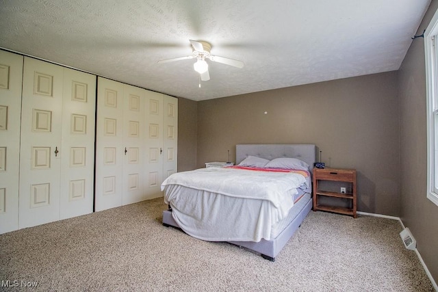 carpeted bedroom with a closet, visible vents, baseboards, a textured ceiling, and a ceiling fan