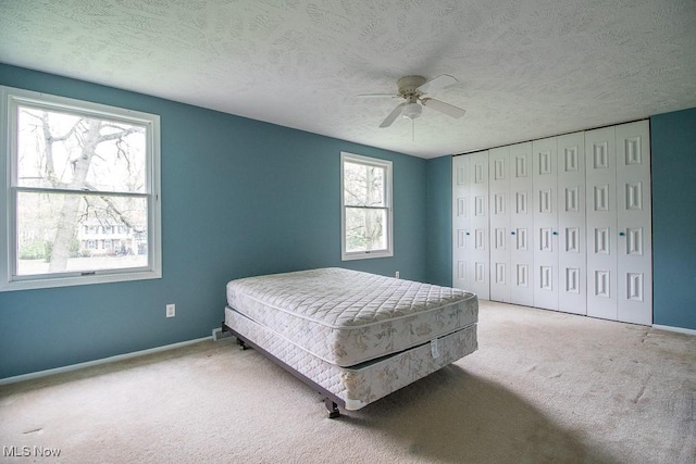 bedroom featuring ceiling fan, a textured ceiling, baseboards, a closet, and carpet flooring