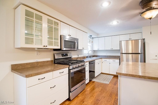 kitchen featuring a sink, appliances with stainless steel finishes, light wood finished floors, and white cabinetry