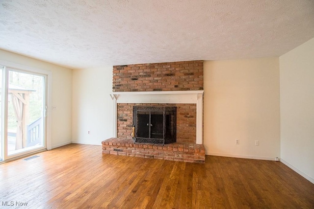 unfurnished living room with a fireplace, a textured ceiling, baseboards, wood finished floors, and visible vents
