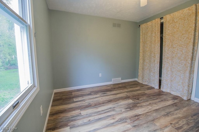 unfurnished bedroom featuring visible vents, multiple windows, and wood finished floors