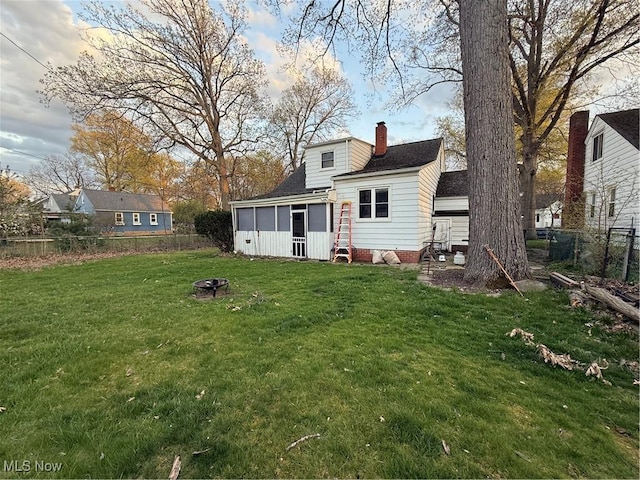 rear view of property featuring a fire pit, a fenced backyard, a chimney, a sunroom, and a yard