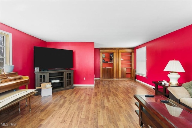 living room featuring plenty of natural light, baseboards, wood finished floors, and built in shelves