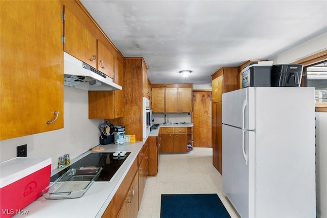 kitchen with freestanding refrigerator, light floors, light countertops, under cabinet range hood, and brown cabinets